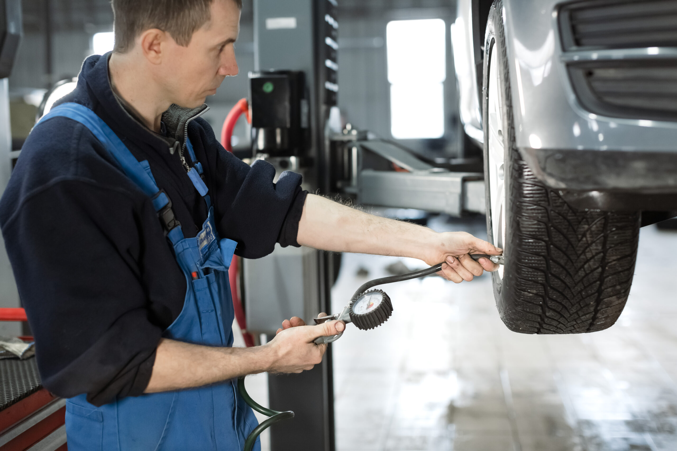 A mechanic is checking the tire pressure at a vehicle’s wheel.